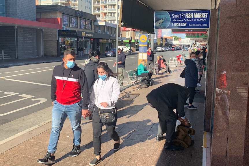 A man and woman walk down a street wearing masks 