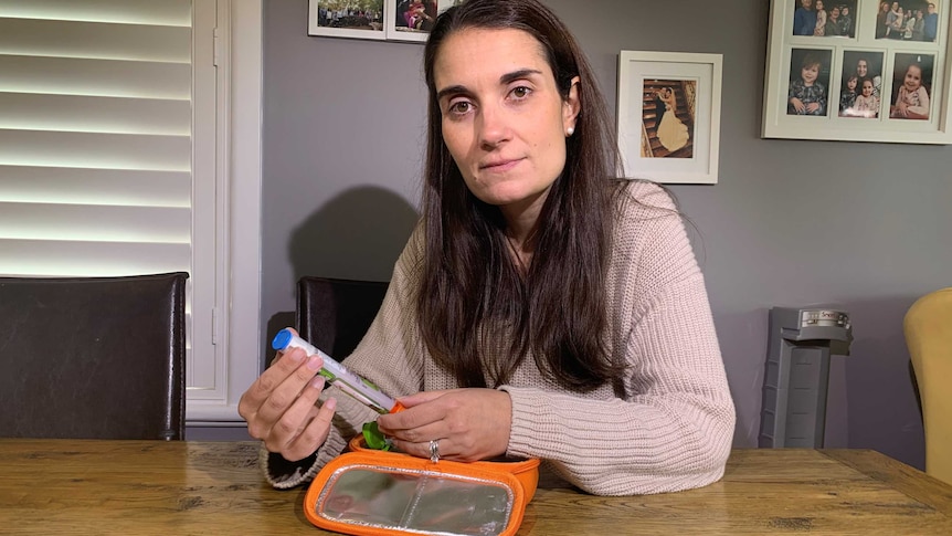 A women holding an drug injection device looks at the camera.