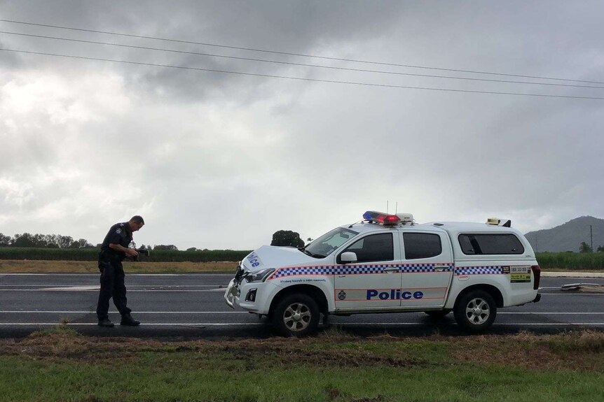 An officer inspects a damaged police car on the side of the road