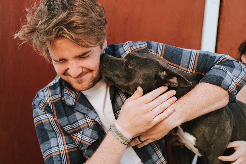 Man hugging his dog, while the dog sniffs his face