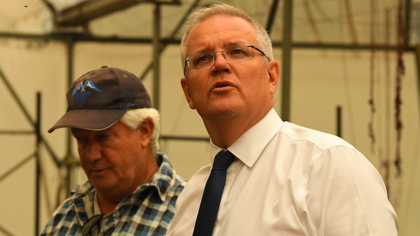 Scott Morrison looks up at the roof of a burnt shed