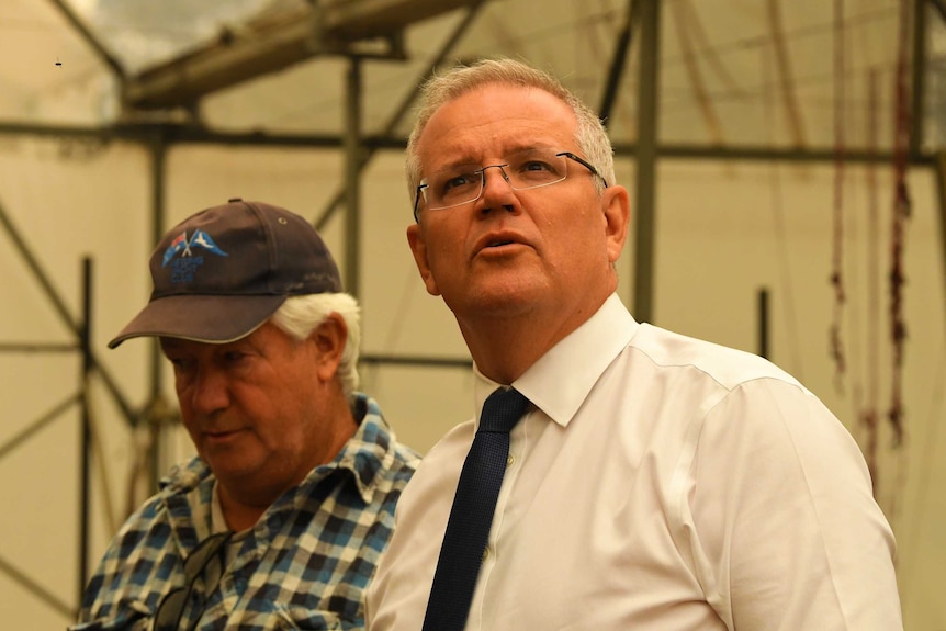 Scott Morrison looks up at the roof of a burnt shed