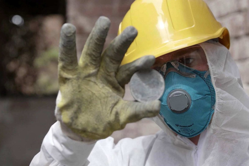 A man in a protective suit and helmet holds up a medal.