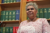 Indigenous female politician stands in office in front of shelf of parliamentary books