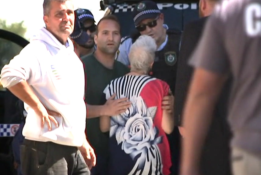 the back of a woman speaking to police while being surrounded by other men