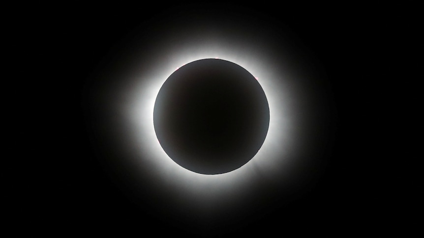 The moon completely covers the sun with only a slither of white light around the circular edge of it against a black sky