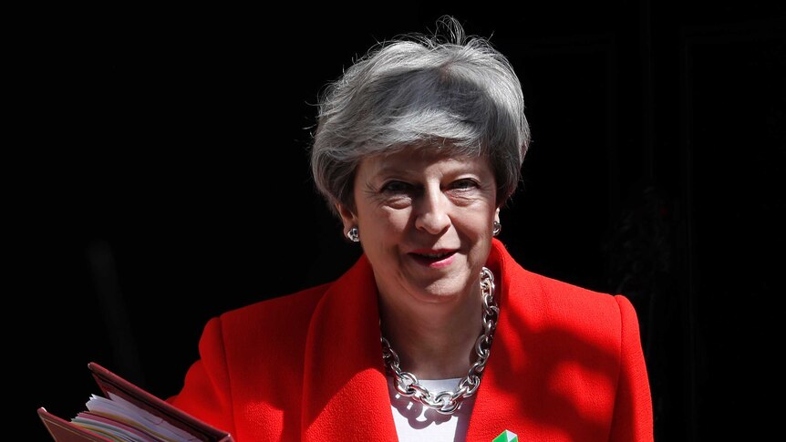 Britain's Prime Minister Theresa May holds a large folder while wearing a red jacket.