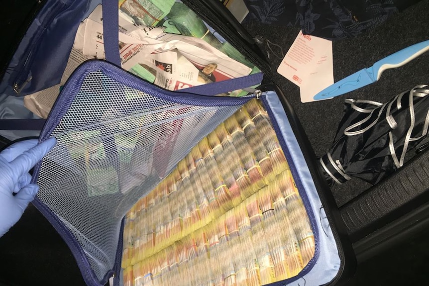 Police open a bag to reveal wads of $50 and $100 notes.