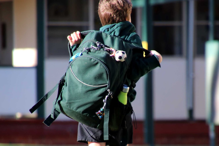 A boy carrying a green backpack arrives at primary school.