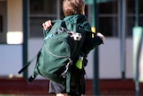 A boy carrying a green backpack arrives at primary school.