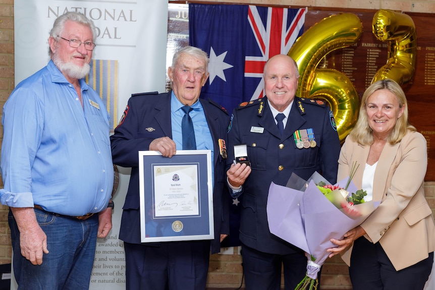 four people standing smiling, one person holding an award 