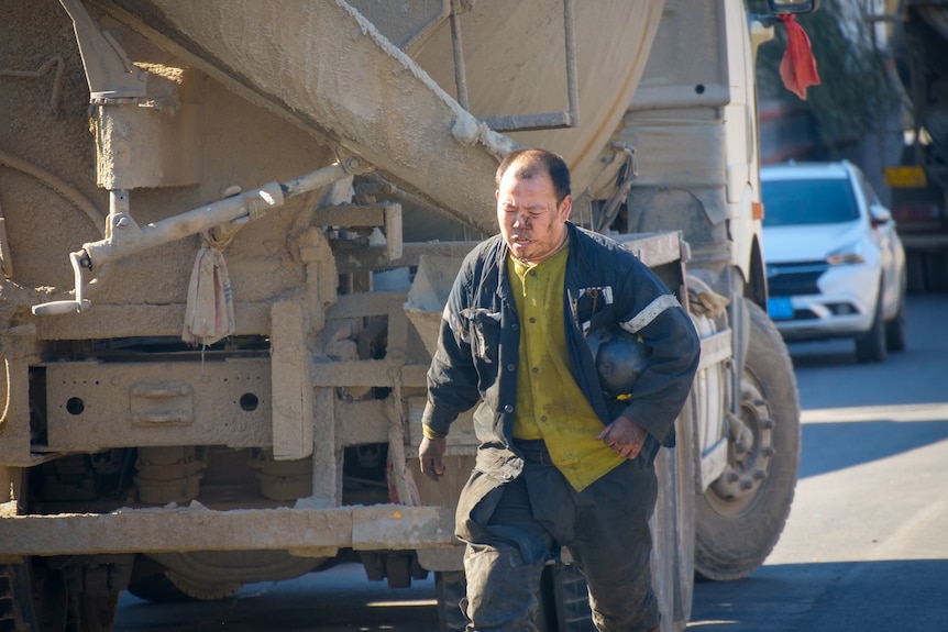 A man with soot on his face walks past a cement truck 