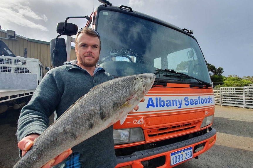 Albany Seafoods owner Bryn Westerberg standing in front of a company-branded truck and holding an Australian salmon