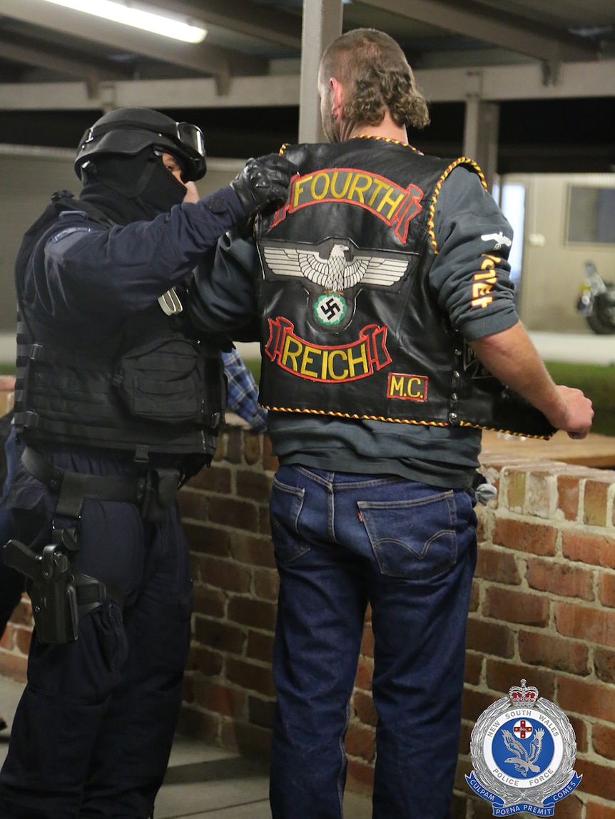 Police arrest a man wearing Fourth Reich bikie colours at a clubhouse