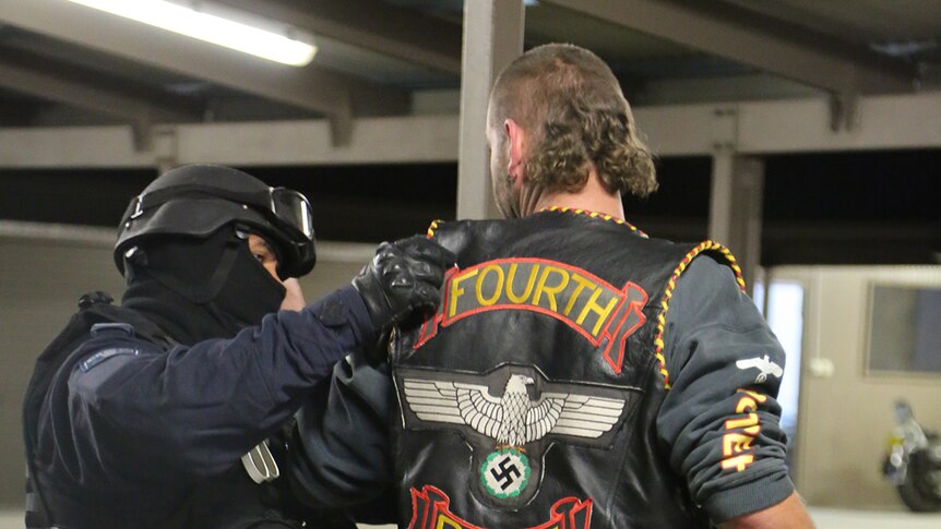 Police arrest a man wearing Fourth Reich bikie colours at a clubhouse