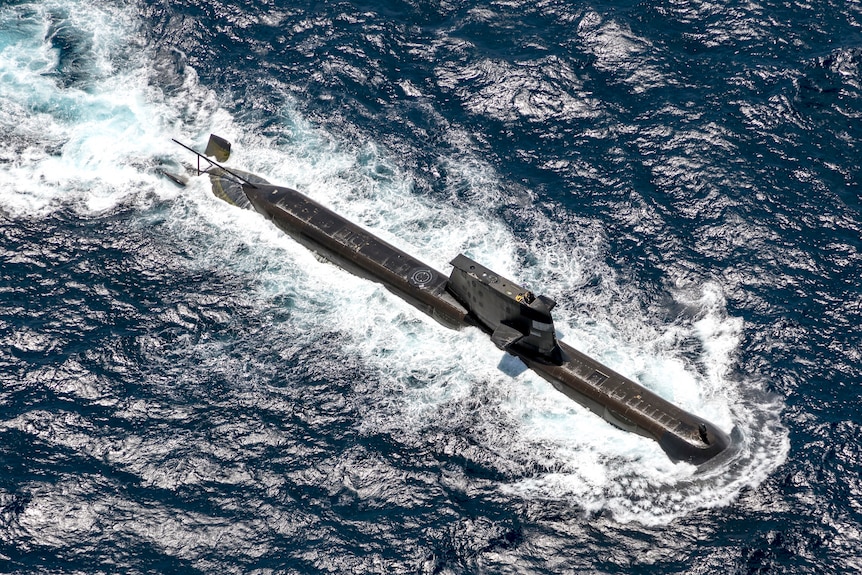 An aerial photograph of a black submarine at the surface of the sea