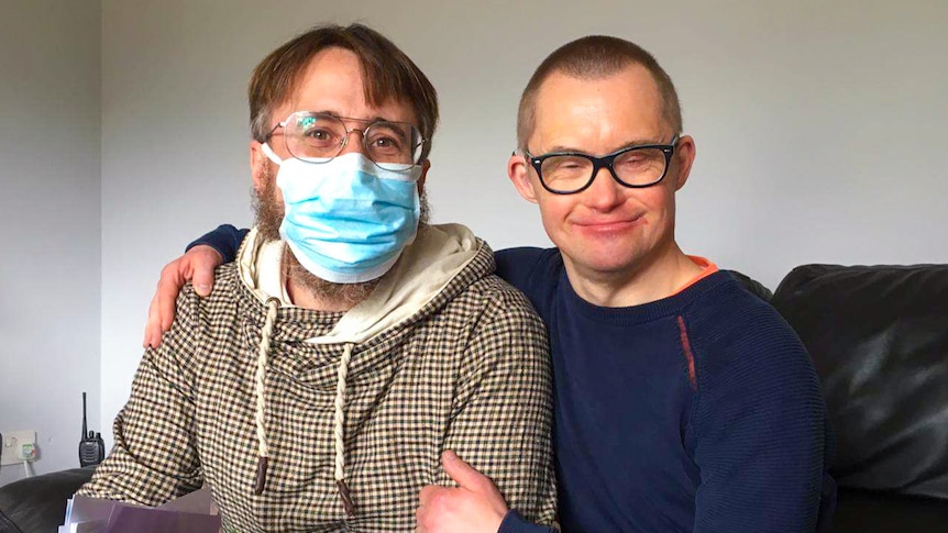 A man in a glasses and a mask sits with a man wearing glasses, who has his arm around him.