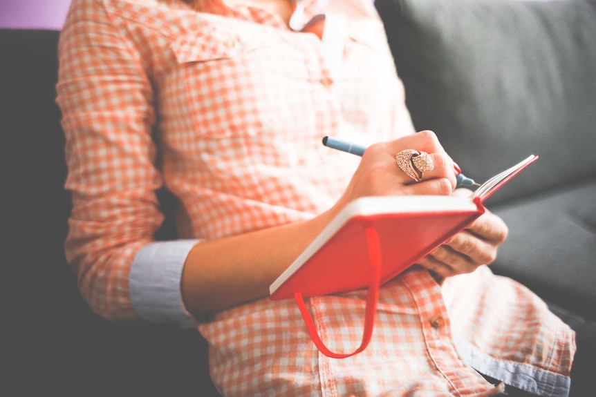 A woman writes in a red notebook.