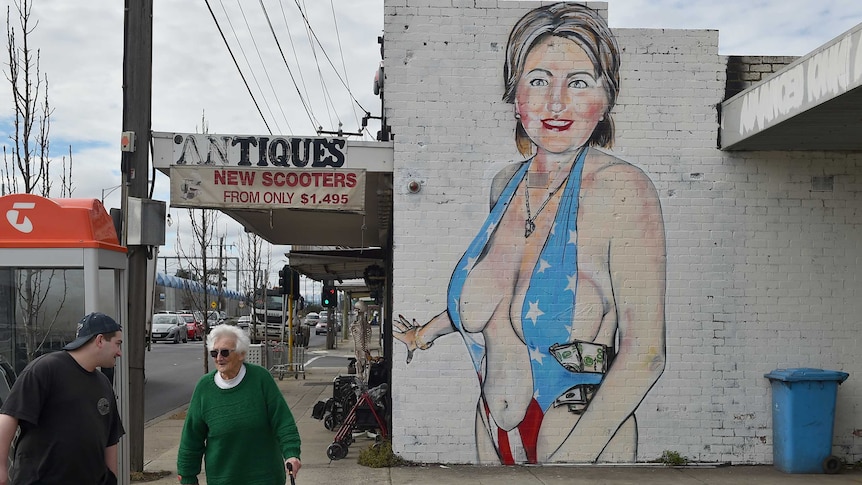 Pedestrians walk past a mural of Democrat US presidential nominee Hillary Clinton clad in a swimsuit