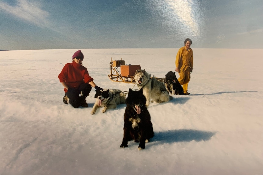 two people in the snow with four husky dogs