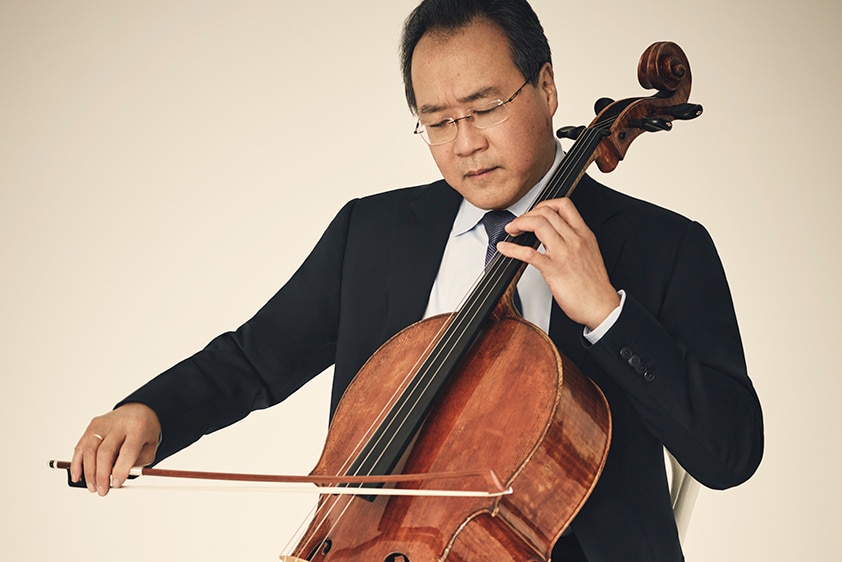 Cellist Yo-Yo Ma plays cello in a black suit. His eyes are closed and his head is tilted toward his cello.