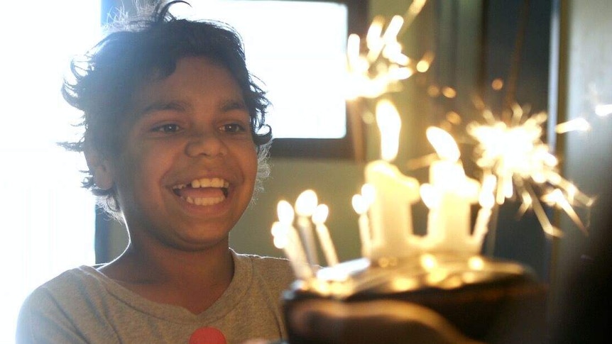 A smiling boy looks at a birthday cake covered in lit candles