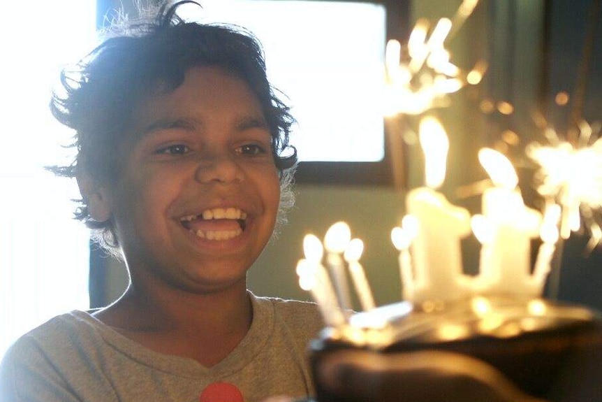 A smiling boy looks at a birthday cake covered in lit candles