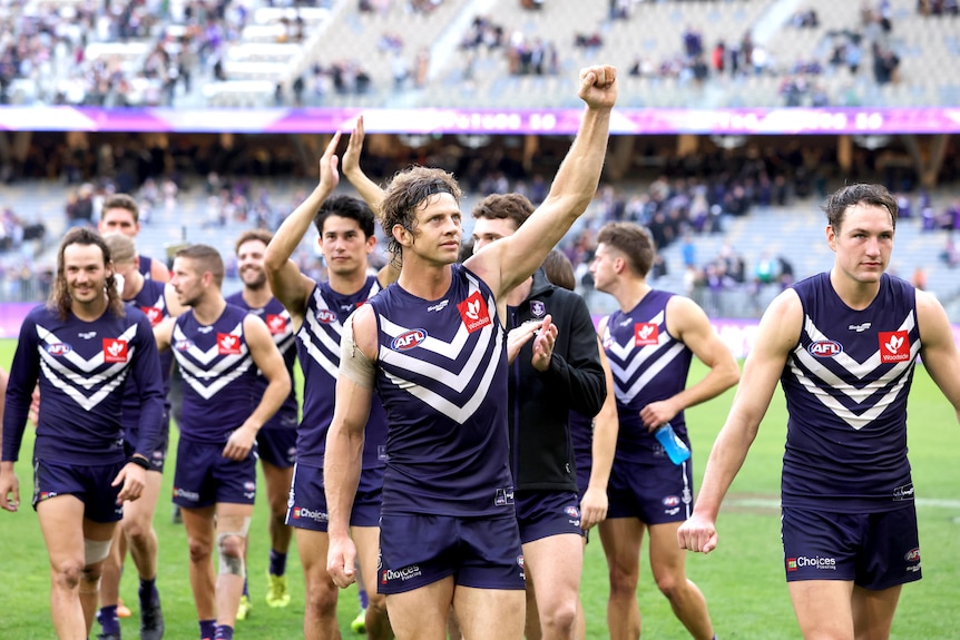 Nat Fyfe is surrounded by team mates as he holds his hand up in celebration