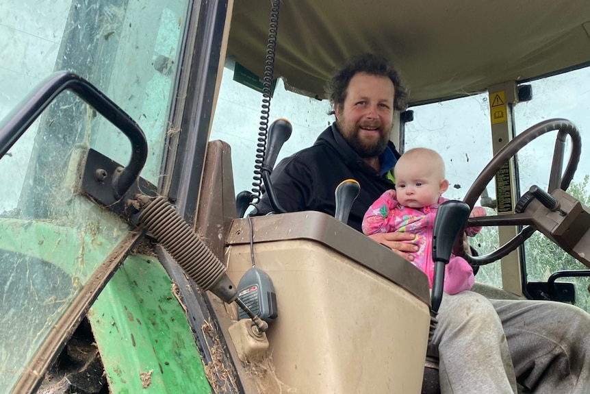 Man and baby daughter in a tractor. He's in a dark pullover and baby's all in pink onesie
