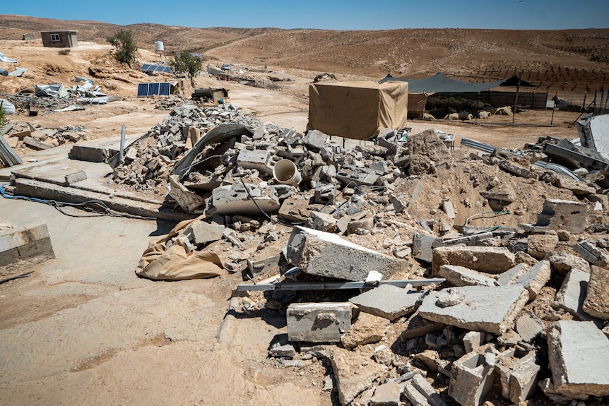 Piles of concrete rubble and debris are scattered across a dusty, rocky desert area