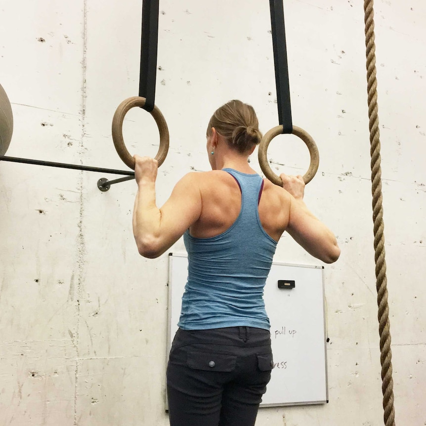 A woman does a pull up on a set of gymnastics rings