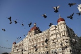 Doves fly in front of Mumbai's Taj Mahal Palace Hotel set against a blue sky.