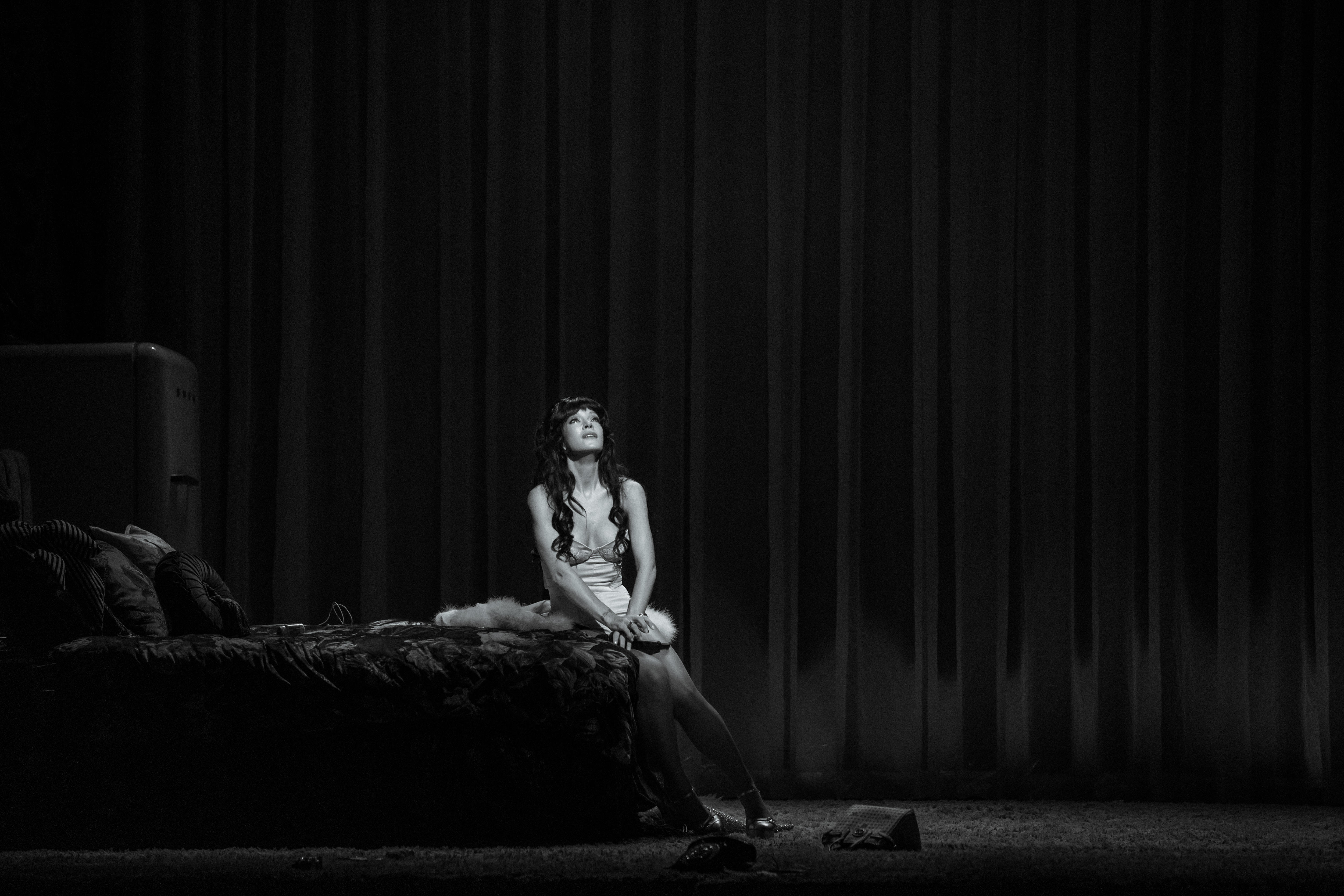 A black and white image of Lily Allen sitting in the middle of a queen sized bed while crying.