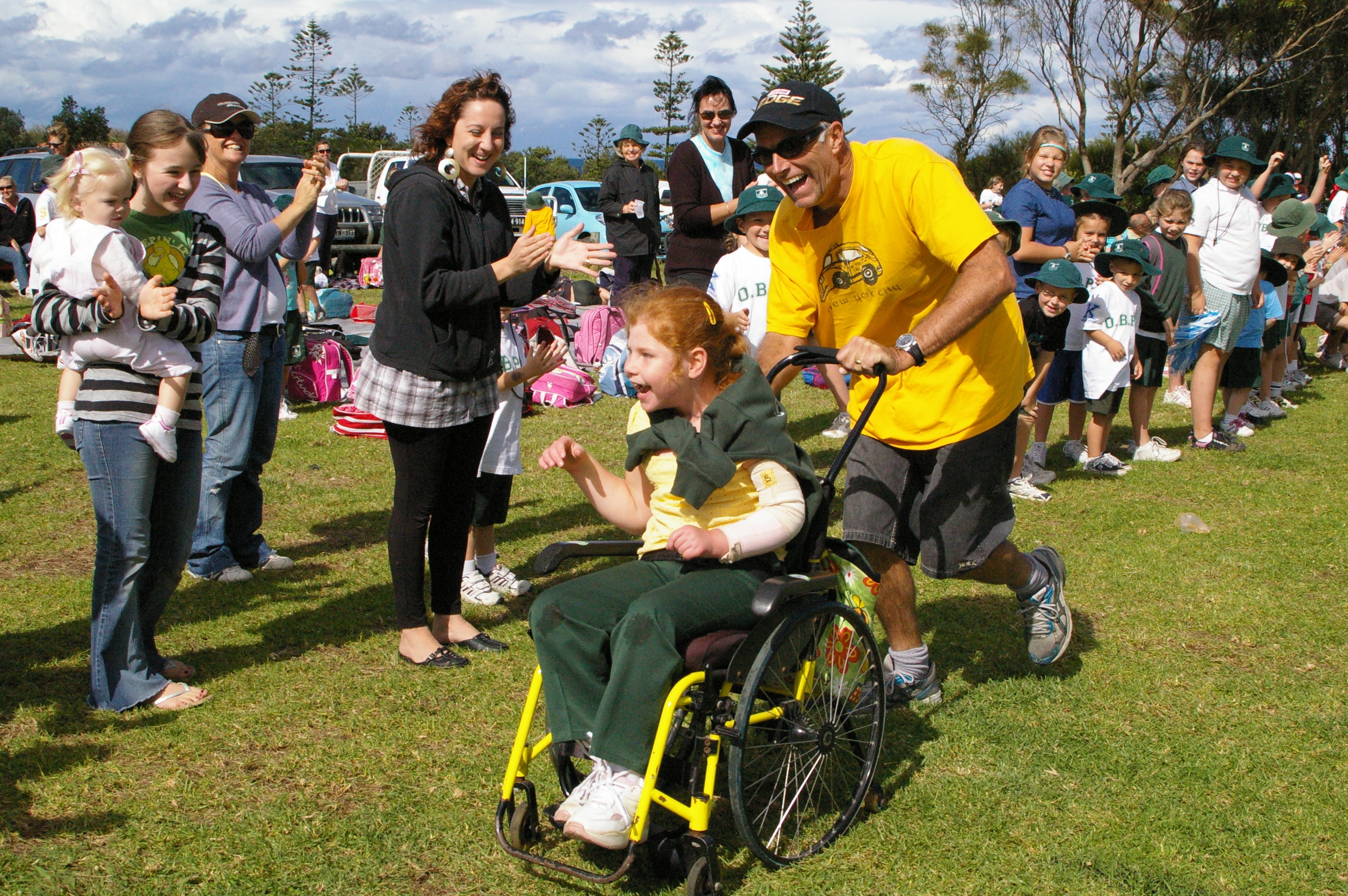 Lillian being pushed along a grass race track in her wheel chair - people lining the edges sheering and clapping her on. 