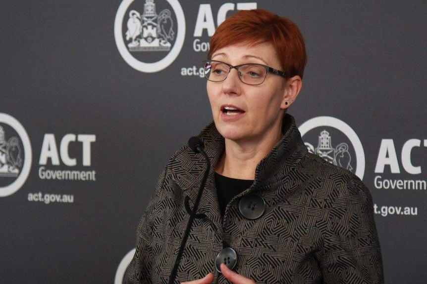 A woman with bright red hair stands at a podium.