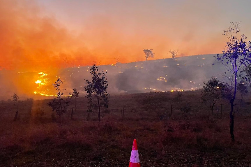 Fire burns on a hill in a devastated landscape at night.