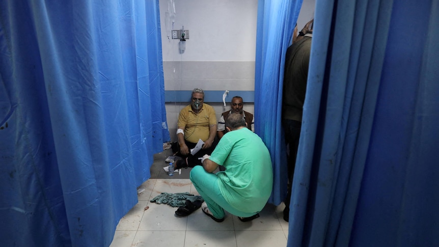 Two men sit on ground while doctor treats them 