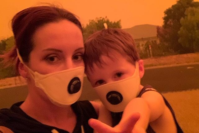 Amy Houghton and her son wearing protective masks against an orange sky in Mallacoota.