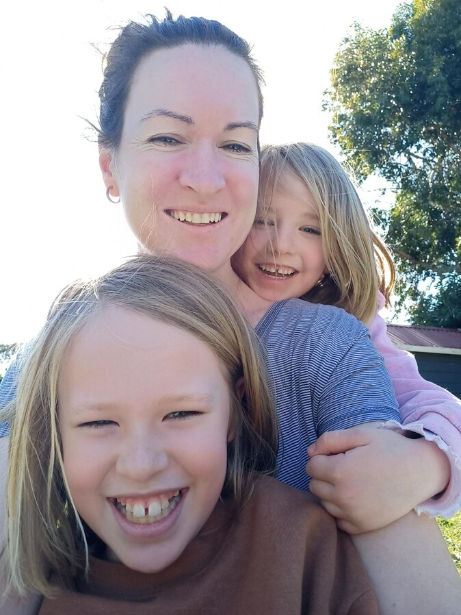 A woman and two girls taking a selfie in the sunshine while smiling.