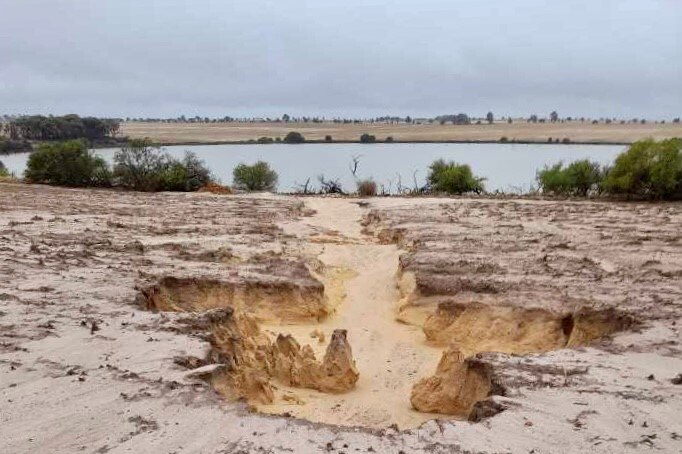 A wet paddock above a dam, with a large crater erosion caused by rainfall