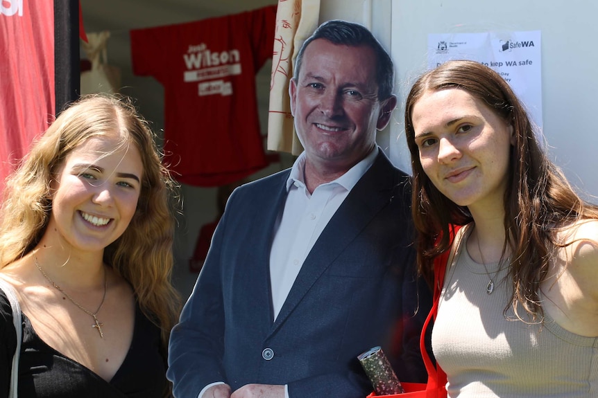 Two young women standing beside a cardboard model of Mark McGowan