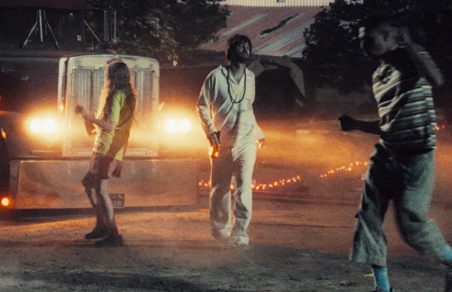 Kevin Parker camina frente a un camión con un traje completamente blanco mientras la gente baila a su alrededor.