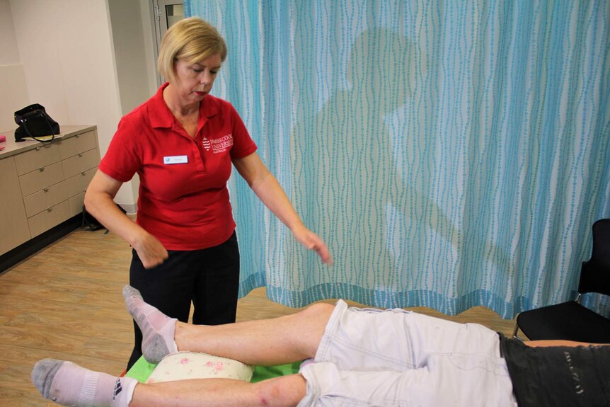 A woman in a red shirt performs healing touch on a man who is lying down