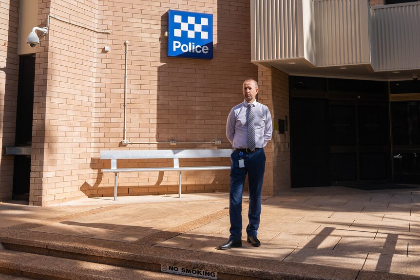 A man in a collared shirt and tie standing outside the Alice Springs courthouse, with a police sign behind him. 