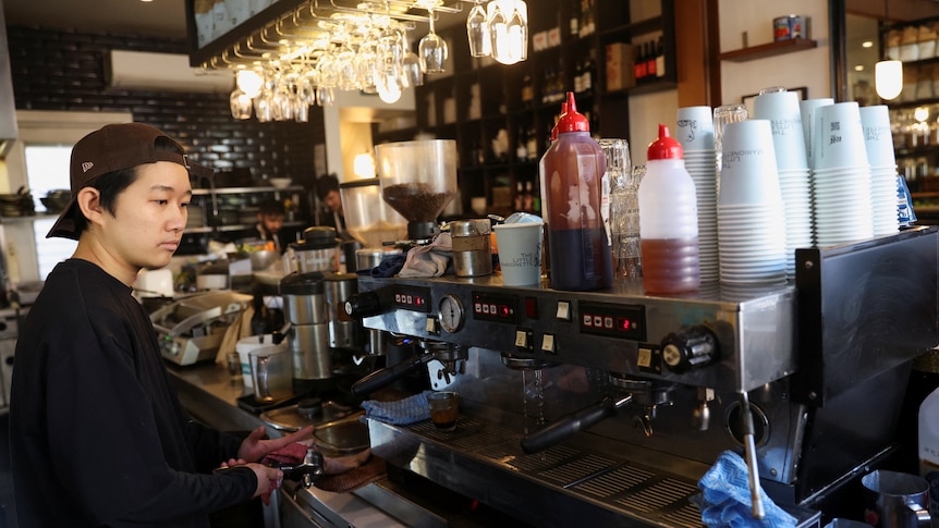 A worker makes a coffee using a commercial machine at Bar Zini 
