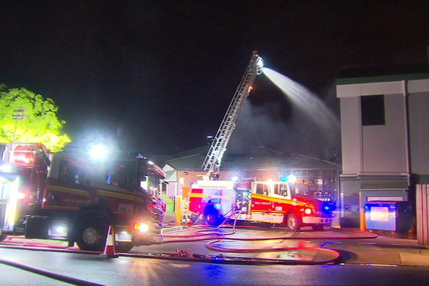 A firefighter at the top of a fire truck ladder sprays water onto a building.