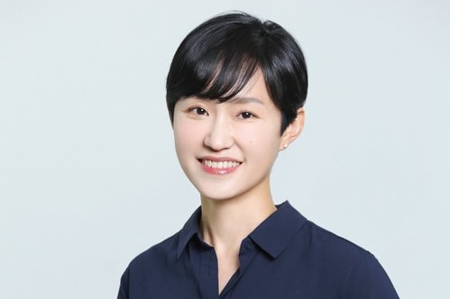 Hawon Jung seen from torso up, wearing dark blue shirt with short black hair, smiling widely.