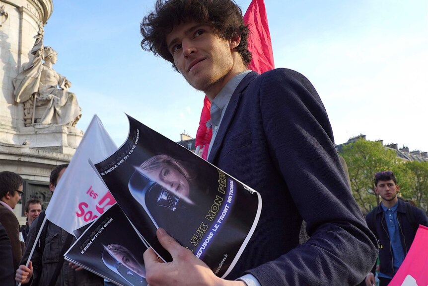 A young frenchman wearing a suit holds images depicting le pen as darth vader from star wars