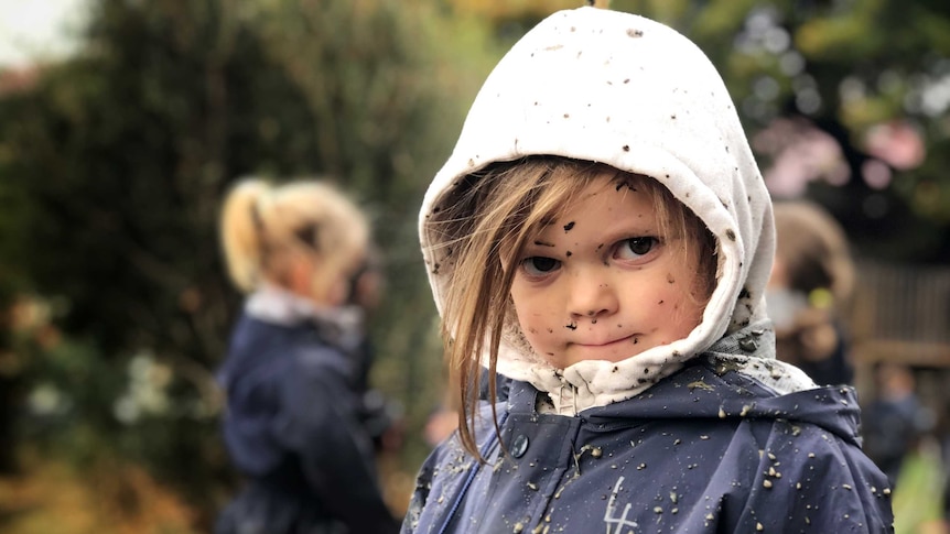 A small mud-splattered child stares at the camera.