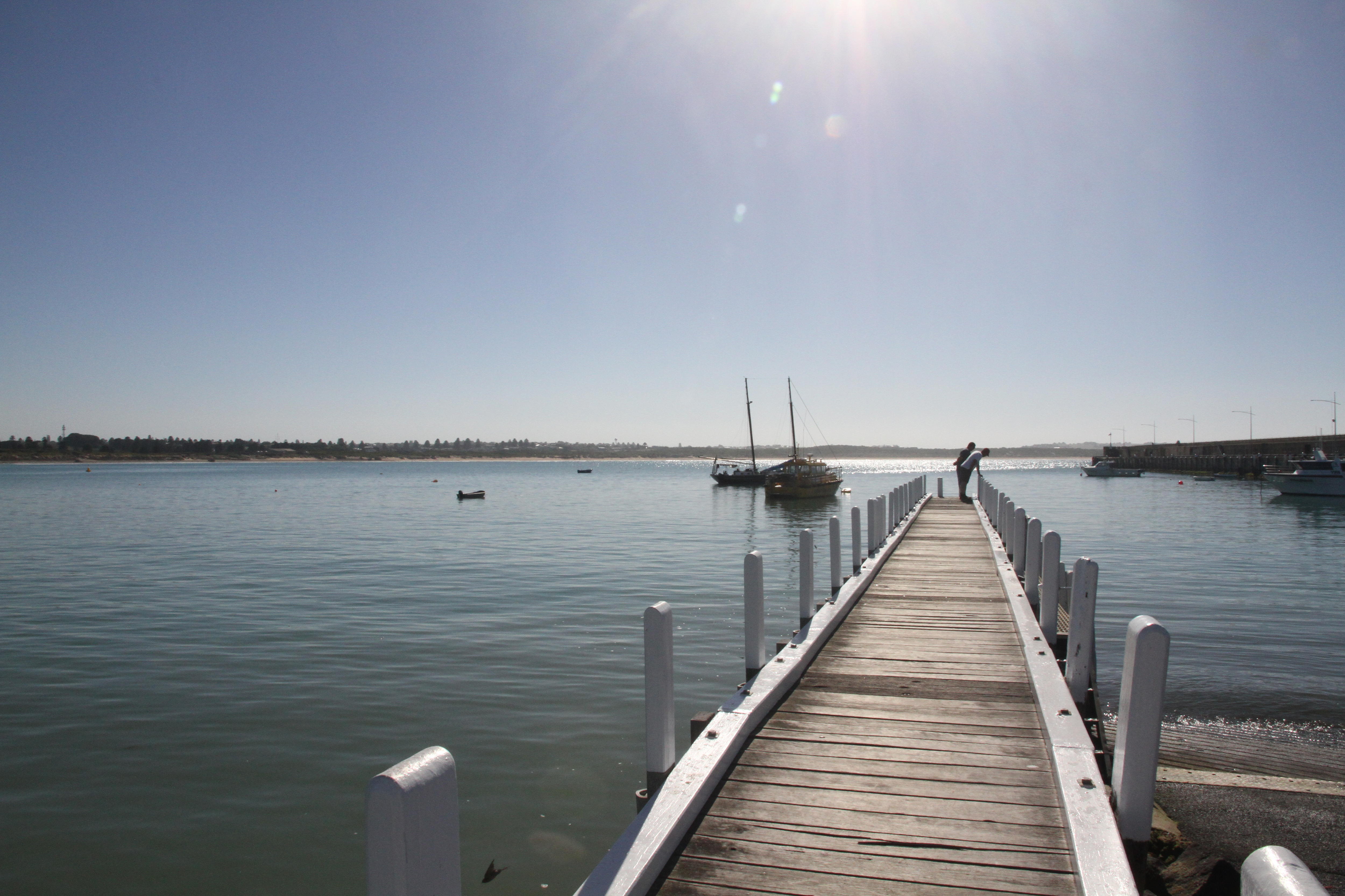 People stand on a wooden jetty jutting out into a sunlit bay.